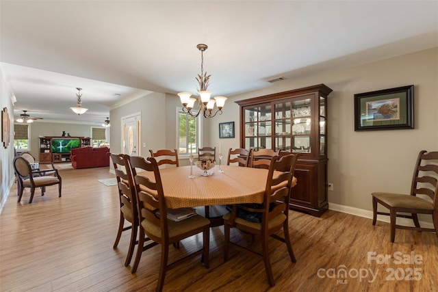 dining area with visible vents, crown molding, baseboards, light wood-style flooring, and ceiling fan with notable chandelier