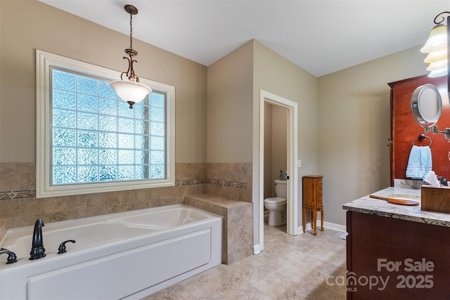 bathroom featuring baseboards, toilet, vanity, and a garden tub