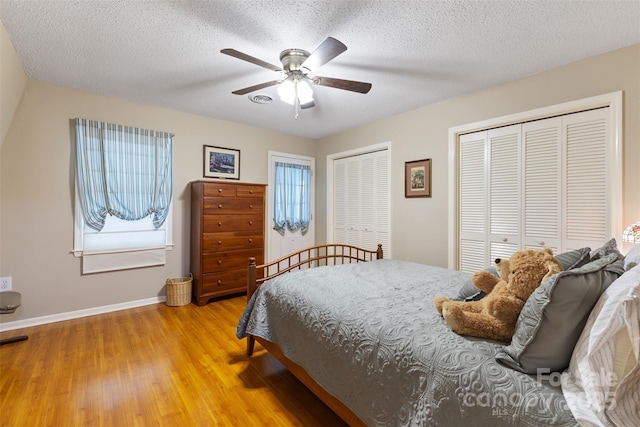 bedroom with light wood finished floors, baseboards, a textured ceiling, and multiple closets