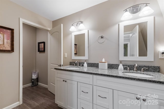 full bath with double vanity, wood finished floors, baseboards, and a sink