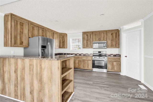 kitchen with a textured ceiling, dark hardwood / wood-style floors, dark stone countertops, and stainless steel appliances