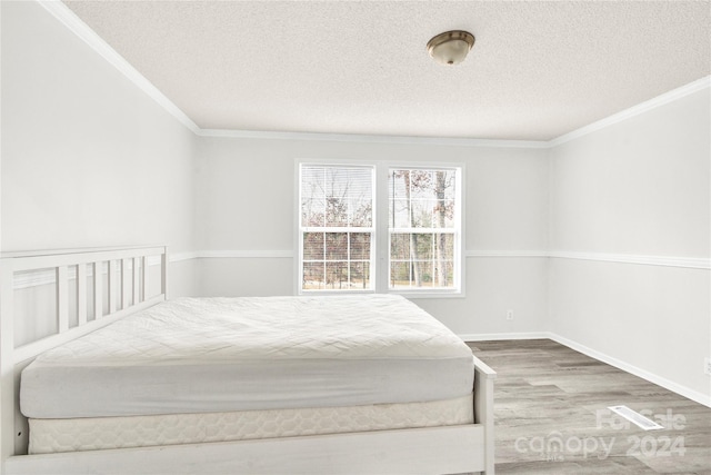 bedroom featuring wood-type flooring, a textured ceiling, and ornamental molding