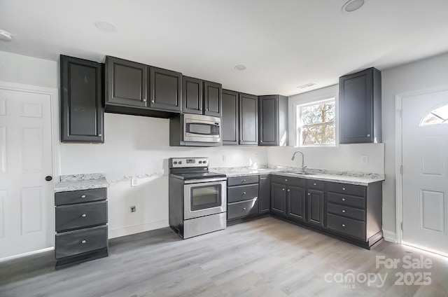 kitchen featuring stainless steel appliances, light stone counters, light hardwood / wood-style floors, and sink