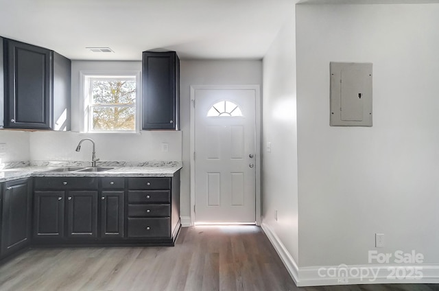 kitchen featuring electric panel, light stone counters, sink, and light hardwood / wood-style flooring