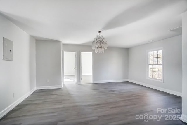 empty room with a notable chandelier, dark wood-type flooring, and electric panel