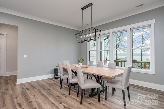 dining space featuring a notable chandelier, crown molding, wood-type flooring, and a water view