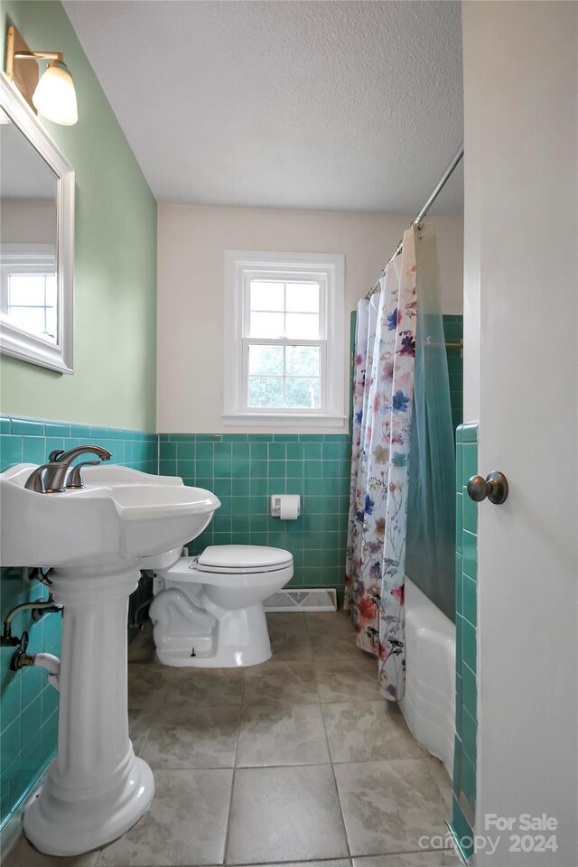 bathroom featuring tile patterned floors, toilet, tile walls, a textured ceiling, and shower / tub combo