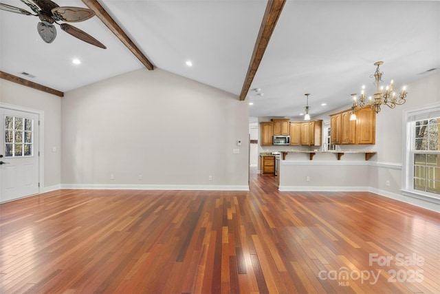 unfurnished living room with ceiling fan with notable chandelier, vaulted ceiling with beams, and dark wood-type flooring