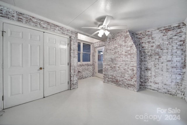 unfurnished bedroom featuring a closet, ceiling fan, and brick wall