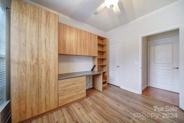 unfurnished office featuring ceiling fan, built in desk, and light hardwood / wood-style flooring