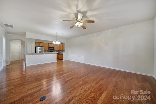 unfurnished living room with ceiling fan with notable chandelier and dark wood-type flooring