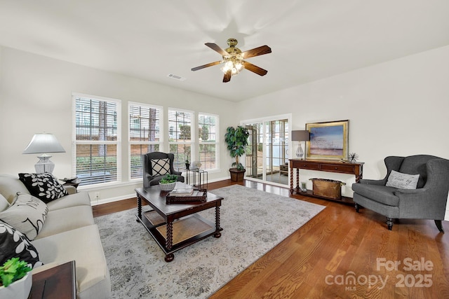 living room with baseboards, wood finished floors, visible vents, and ceiling fan