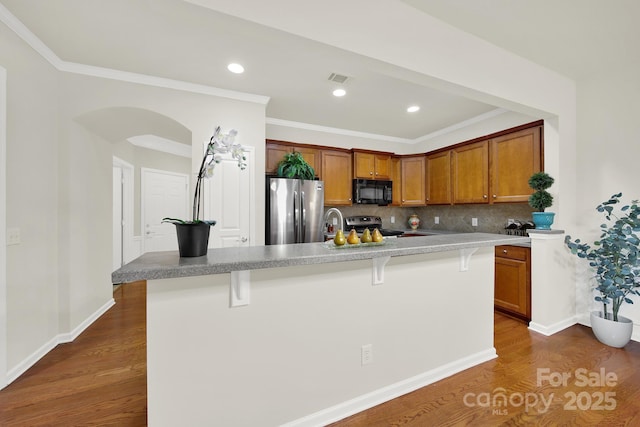 kitchen featuring a kitchen island with sink, a kitchen breakfast bar, dark wood finished floors, stainless steel appliances, and decorative backsplash