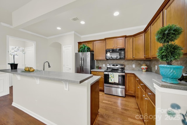 kitchen featuring stainless steel appliances, visible vents, wood finished floors, and brown cabinetry