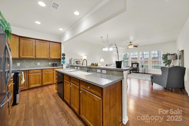 kitchen with backsplash, dishwasher, brown cabinets, wood finished floors, and a sink