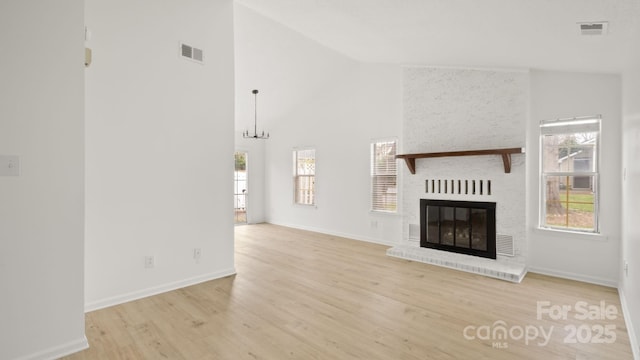 unfurnished living room featuring high vaulted ceiling, light wood finished floors, a fireplace, and visible vents