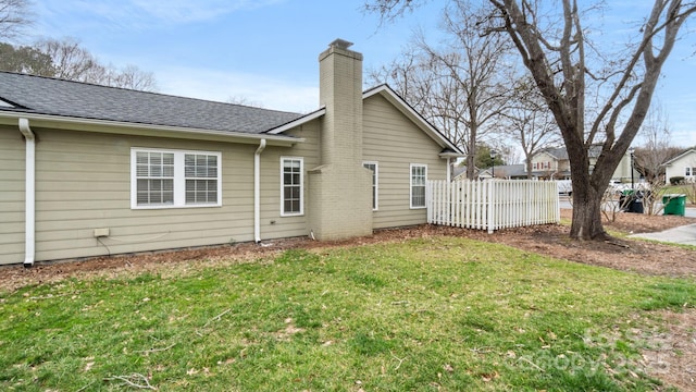 rear view of house with a yard, roof with shingles, fence, and a chimney