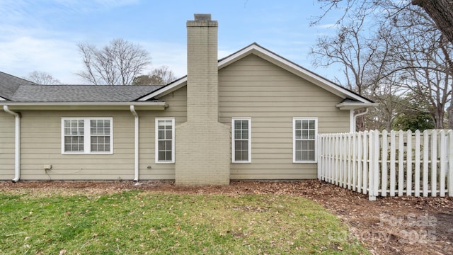 rear view of house with a shingled roof, a chimney, fence, and a lawn