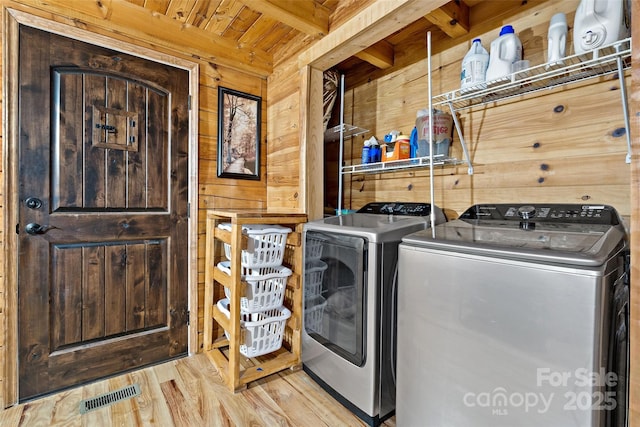 laundry room with washing machine and dryer, light hardwood / wood-style flooring, wood ceiling, and wood walls