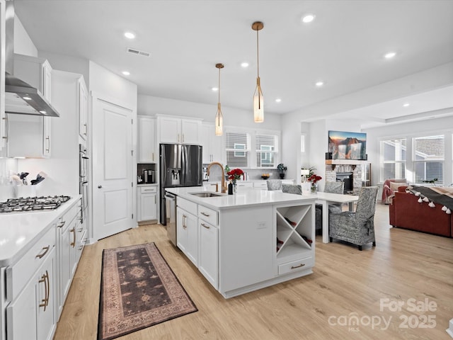 kitchen featuring pendant lighting, light countertops, white cabinetry, an island with sink, and wall chimney exhaust hood