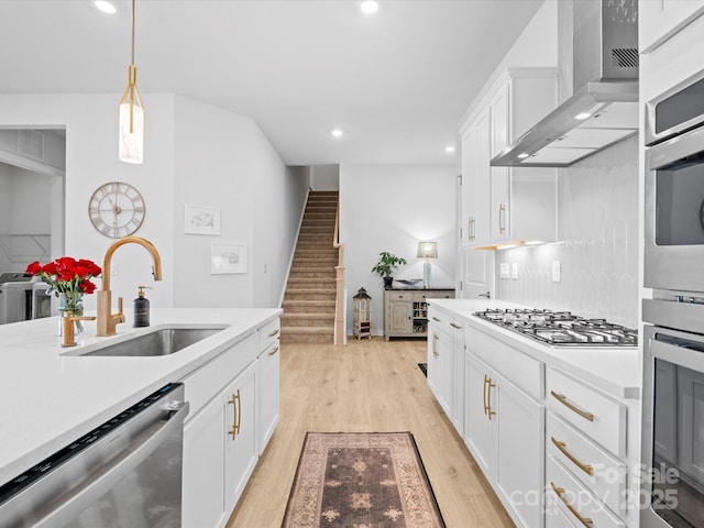 kitchen featuring light countertops, appliances with stainless steel finishes, white cabinets, a sink, and wall chimney exhaust hood