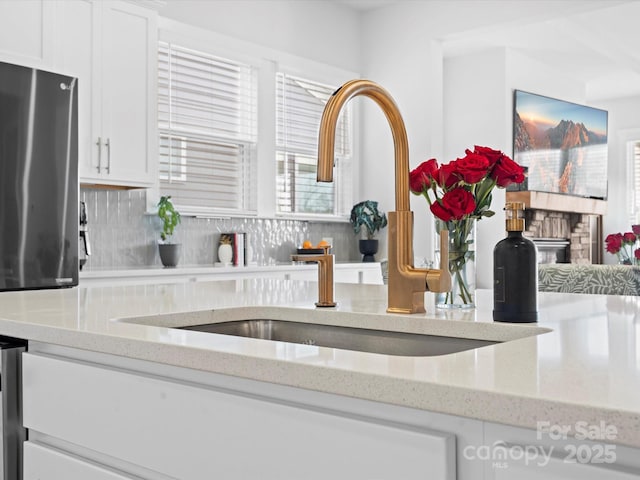 details featuring light stone counters, white cabinets, a sink, and backsplash