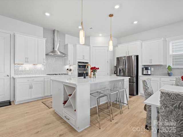 kitchen featuring wall chimney range hood, white cabinetry, stainless steel appliances, and light countertops