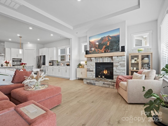 living area with light wood-style floors, recessed lighting, visible vents, and a stone fireplace