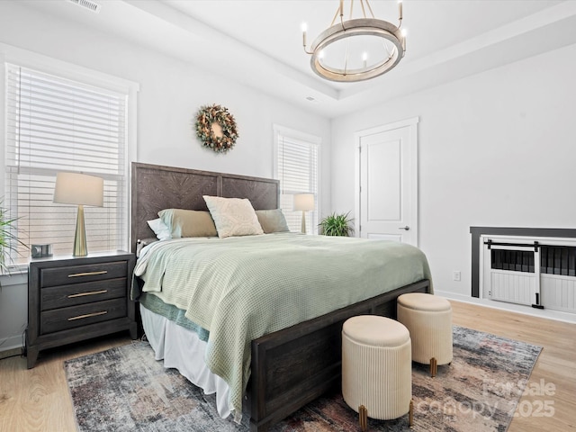 bedroom featuring light wood finished floors, baseboards, a raised ceiling, and an inviting chandelier