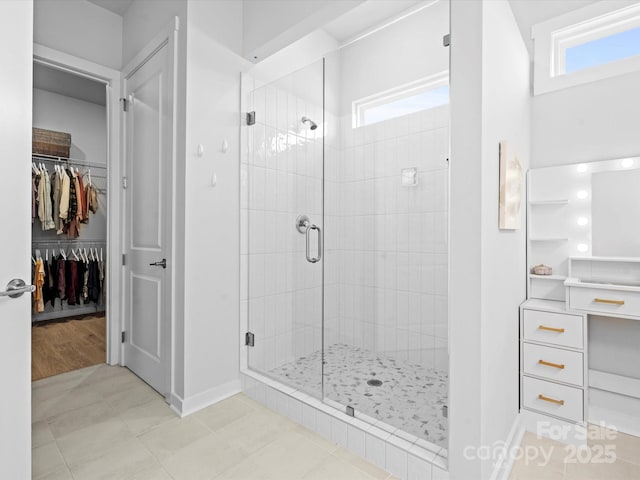 bathroom with a shower stall, a spacious closet, baseboards, and tile patterned floors