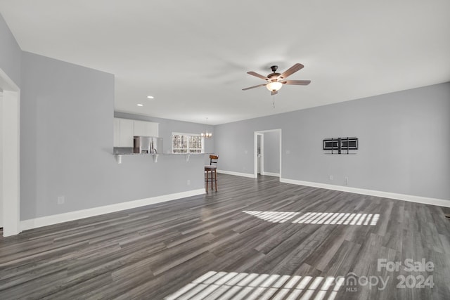 unfurnished living room featuring ceiling fan with notable chandelier and dark wood-type flooring