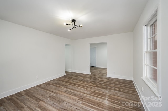 empty room featuring an inviting chandelier, baseboards, and wood finished floors