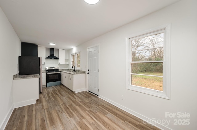 kitchen with appliances with stainless steel finishes, light wood-style floors, white cabinets, a sink, and wall chimney exhaust hood