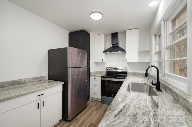 kitchen featuring light wood finished floors, stainless steel appliances, wall chimney range hood, open shelves, and a sink