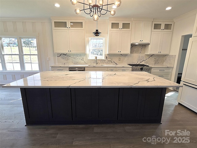 kitchen with light stone counters, sink, a kitchen island, and hanging light fixtures