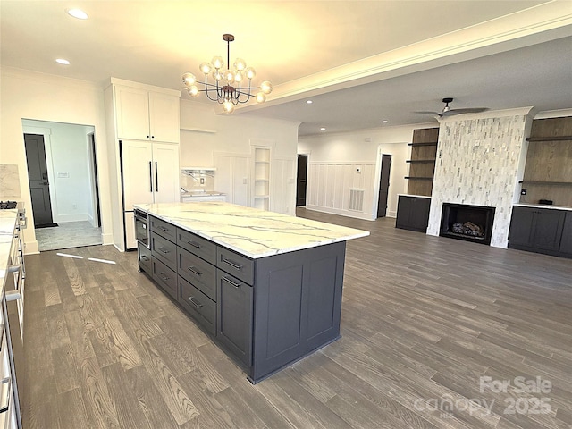 kitchen with pendant lighting, white cabinetry, light stone countertops, a kitchen island, and a stone fireplace