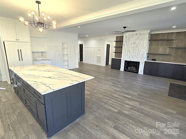 kitchen featuring decorative light fixtures, a fireplace, light stone countertops, ceiling fan with notable chandelier, and white cabinets