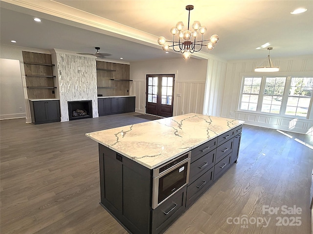 kitchen featuring ceiling fan with notable chandelier, a center island, light stone counters, decorative light fixtures, and french doors