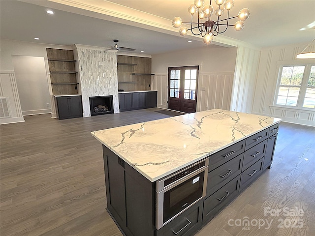 kitchen with pendant lighting, light stone countertops, a kitchen island, ceiling fan with notable chandelier, and french doors