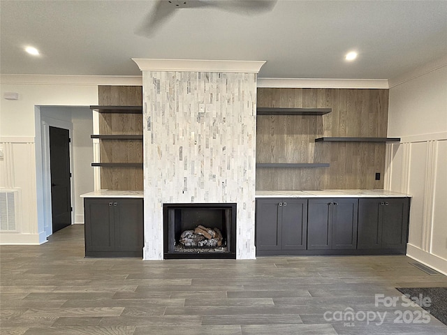 unfurnished living room featuring dark wood-type flooring, ceiling fan, a fireplace, ornamental molding, and built in shelves