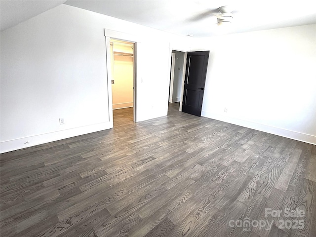 unfurnished bedroom with dark wood-type flooring, a walk in closet, a closet, and ceiling fan