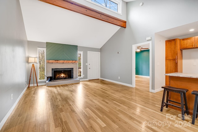 living room with ceiling fan, beamed ceiling, high vaulted ceiling, a fireplace, and light wood-type flooring