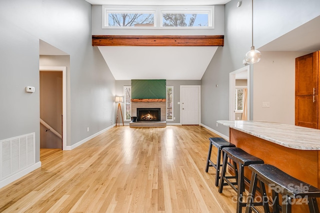 living room featuring a large fireplace, beam ceiling, high vaulted ceiling, and light hardwood / wood-style flooring