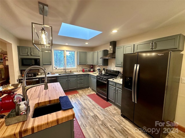 kitchen with a skylight, sink, wall chimney exhaust hood, pendant lighting, and black appliances