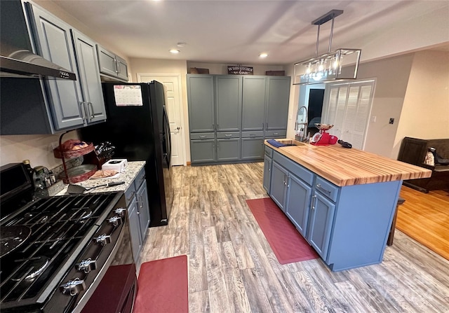 kitchen featuring sink, high end stainless steel range oven, wall chimney range hood, wood counters, and light hardwood / wood-style floors