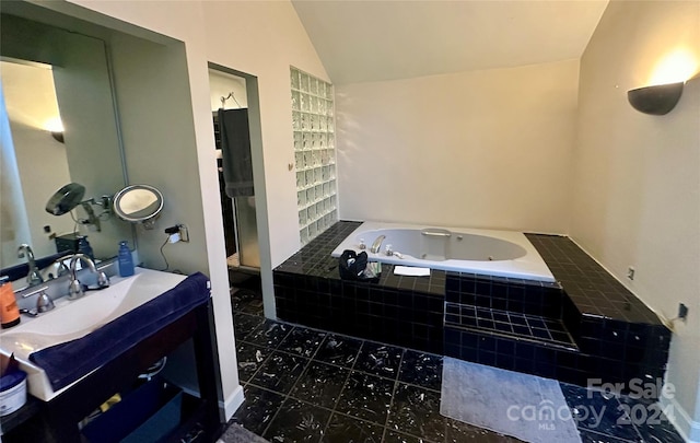 bathroom featuring tile patterned flooring, a relaxing tiled tub, vanity, and vaulted ceiling