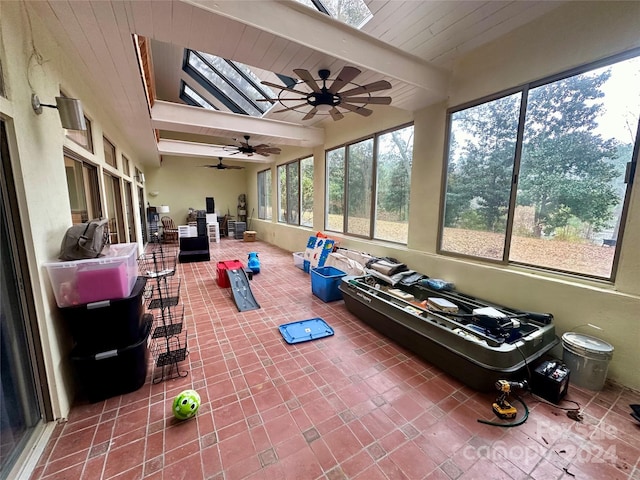 sunroom / solarium featuring a skylight, ceiling fan, and beamed ceiling