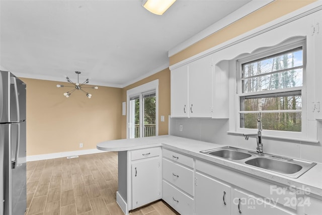 kitchen with white cabinetry, sink, kitchen peninsula, stainless steel fridge, and ornamental molding