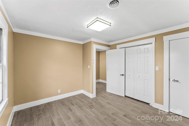 unfurnished bedroom with light hardwood / wood-style floors, ornamental molding, and a textured ceiling