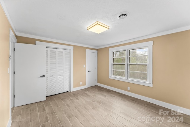 unfurnished bedroom featuring multiple closets, light hardwood / wood-style floors, and ornamental molding